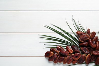 Photo of Tasty sweet dried dates with palm leaf on white wooden table, flat lay. Space for text