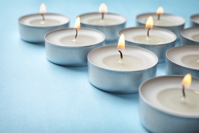 Photo of Small wax candles burning on color background, closeup