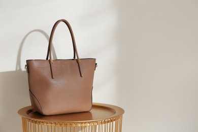 Photo of Stylish leather woman's bag on table near light wall. Space for text