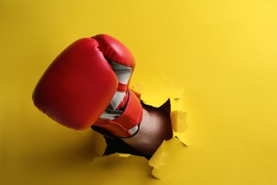 Photo of Man breaking through yellow paper with boxing glove, closeup. Space for text