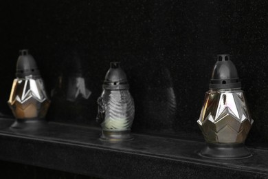 Photo of Different grave lanterns on black tombstone. Funeral ceremony