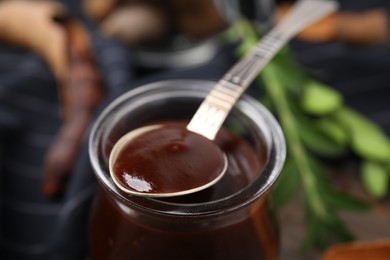 Photo of Jar and spoon of tasty tamarind sauce on table, closeup