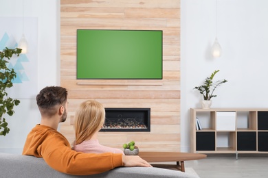 Photo of Couple watching TV on sofa in living room with decorative fireplace