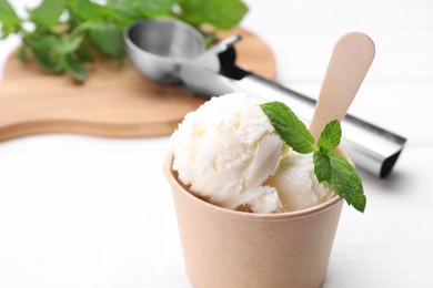 Photo of Delicious vanilla ice cream and mint in paper cup on white table, closeup. Space for text