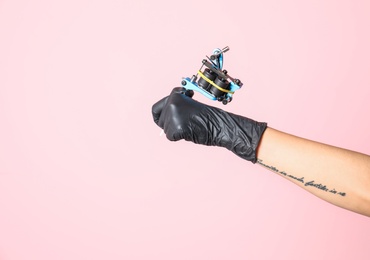 Photo of Professional tattoo artist with machine on color background, closeup. Space for text