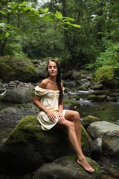 Photo of Beautiful young woman sitting on rock near mountain river in forest