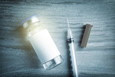 Image of Medication in glass vial and syringe on wooden table, flat lay with space for text. Color toned