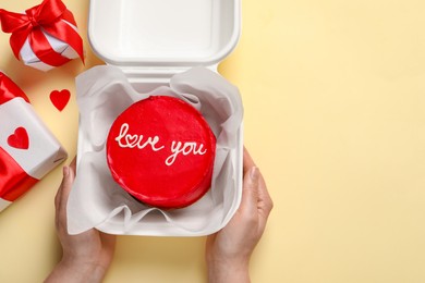 Photo of Woman holding takeaway box with bento cake at beige table, top view. St. Valentine's day surprise