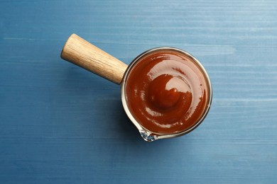 Photo of Tasty barbeque sauce on blue wooden table, top view