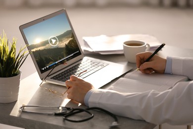 Image of Doctor watching video on laptop at office desk, closeup. Man choosing vacation spots
