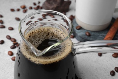 Photo of Turkish coffee in glass cezve and beans on light grey table, closeup