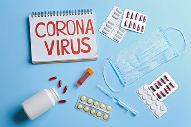 Photo of Flat lay composition of medications and notebook with words CORONA VIRUS on light blue background