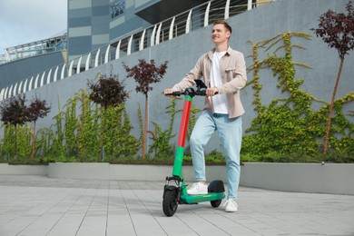 Photo of Happy man with modern electric kick scooter on city street, space for text