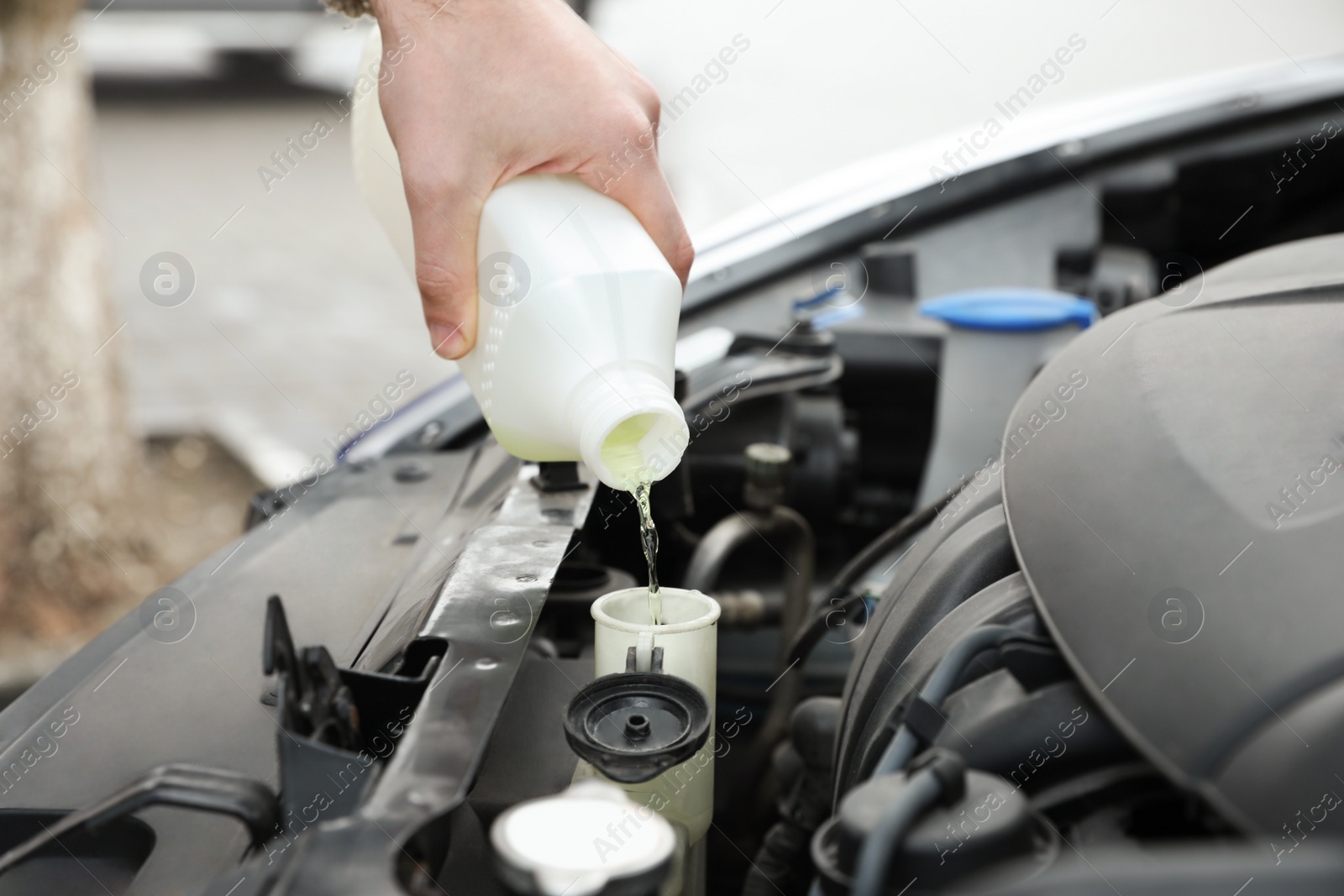 Photo of Man filling car radiator with antifreeze outdoors, closeup