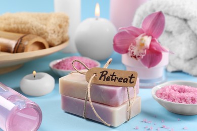 Photo of Retreat concept. Composition with card, different spa products and burning candles on light blue background, closeup
