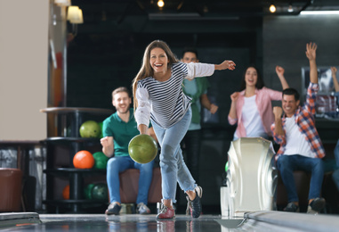 Photo of Young woman throwing ball and spending time with friends in bowling club