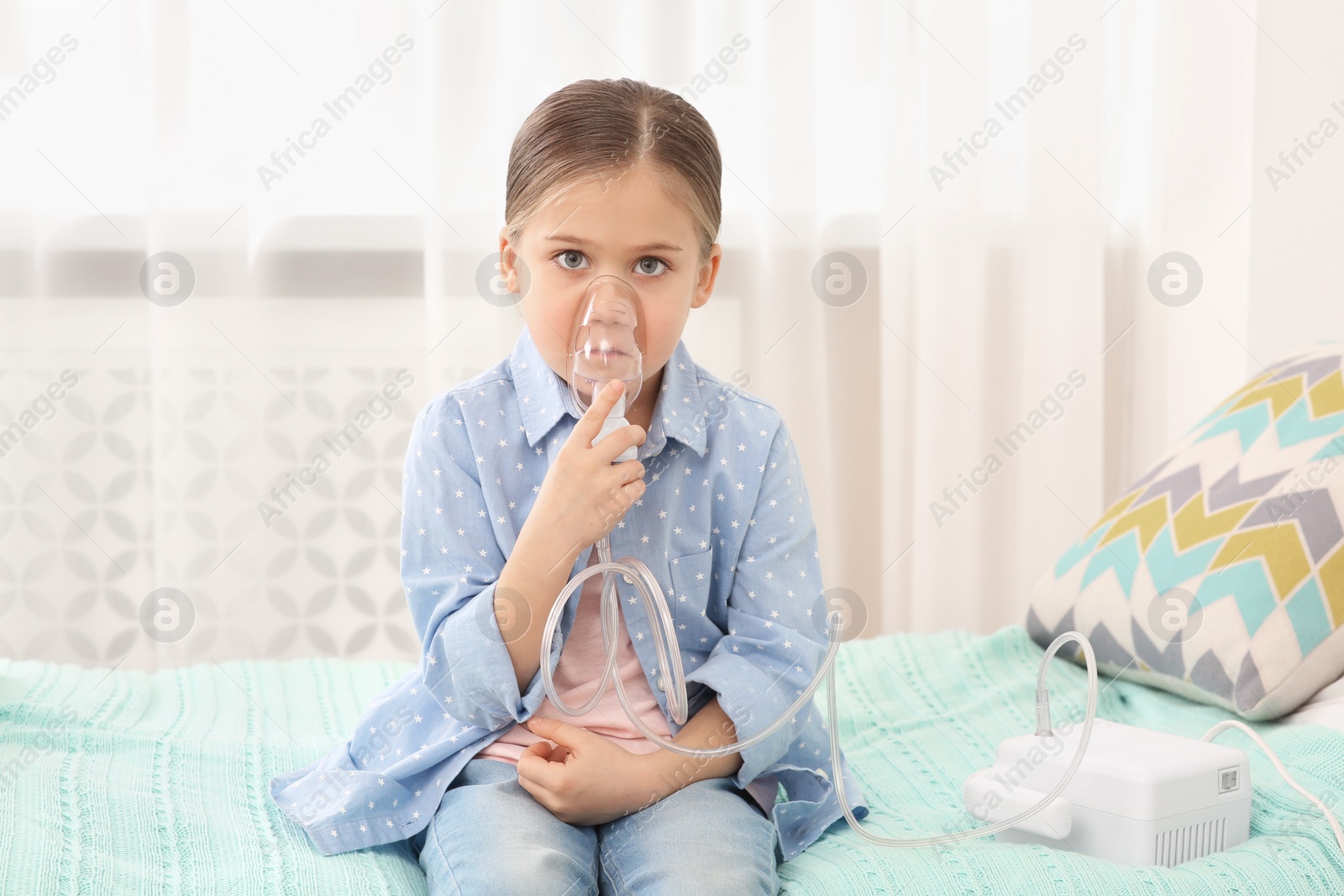 Photo of Sick little girl using nebulizer for inhalation on bed at home