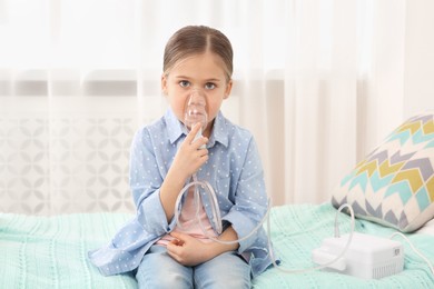 Photo of Sick little girl using nebulizer for inhalation on bed at home