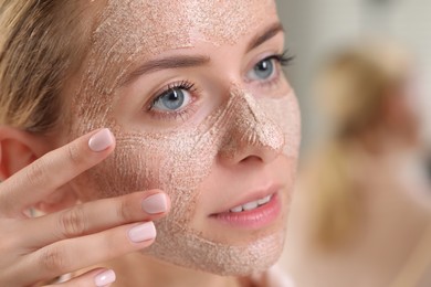 Photo of Woman applying face mask on blurred background, closeup. Spa treatments
