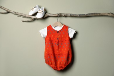 Photo of Baby bodysuit and booties on decorative branch near beige wall