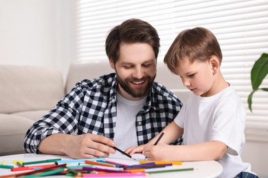 Photo of Happy dad and son drawing together at table indoors