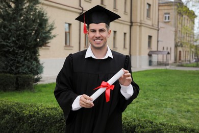 Photo of Happy student with diploma after graduation ceremony outdoors