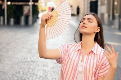 Woman with hand fan suffering from heat outdoors
