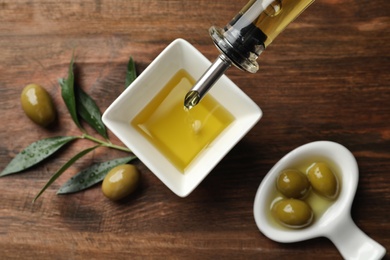 Photo of Pouring fresh olive oil into bowl on table, top view
