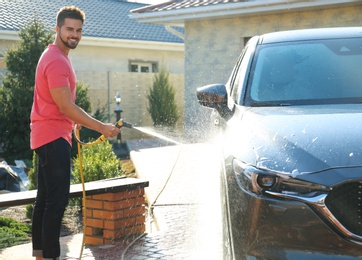 Photo of Young happy man washing car at backyard on sunny day