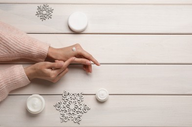 Photo of Woman applying cream onto hand at white wooden table, top view. Space for text
