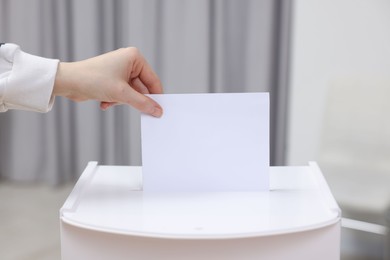Photo of Woman putting her vote into ballot box on blurred background, closeup