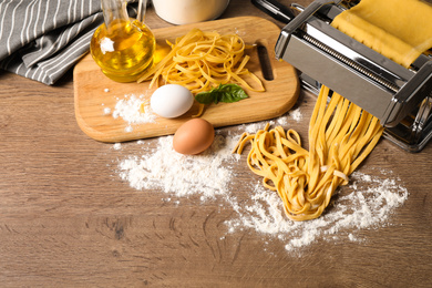 Photo of Pasta maker machine with dough and products on wooden table, above view