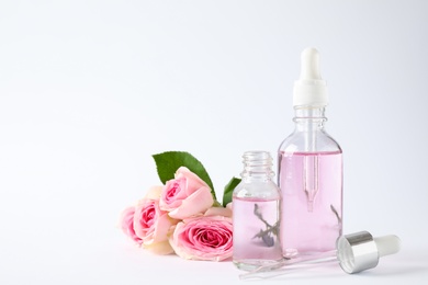 Photo of Bottles of essential oil and roses on white background