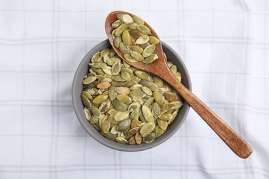 Photo of Bowl with pumpkin seeds and wooden spoon on tablecloth, top view