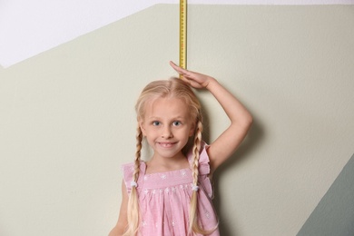 Little girl measuring her height near color wall