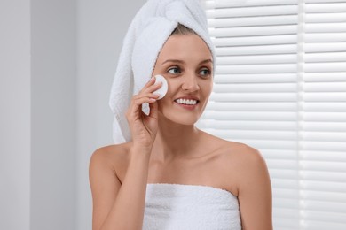 Photo of Young woman cleaning her face with cotton pad indoors