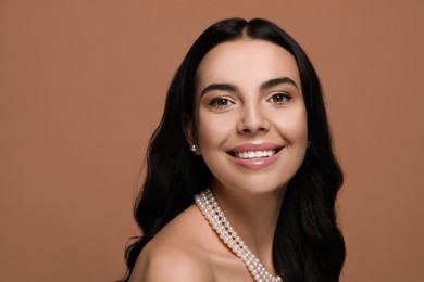 Photo of Young woman wearing elegant pearl jewelry on brown background, space for text