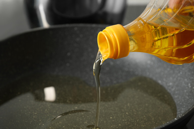 Photo of Pouring cooking oil from bottle into frying pan, closeup