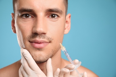 Photo of Man getting facial injection on light blue background, closeup. Cosmetic surgery