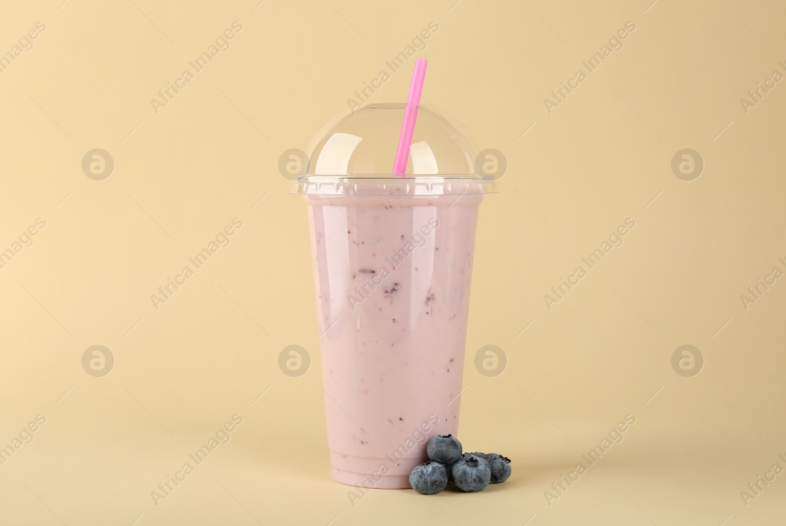 Photo of Plastic cup of tasty smoothie and fresh blueberries on beige background