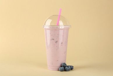 Photo of Plastic cup of tasty smoothie and fresh blueberries on beige background