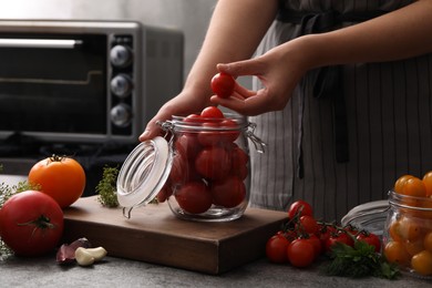 Photo of Woman putting tomatoes into glass jar at kitchen table, closeup. Pickling vegetables