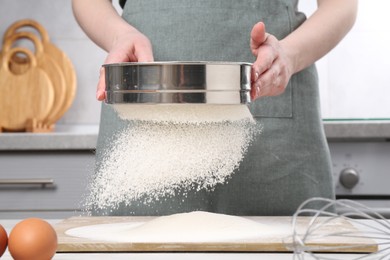 Photo of Woman sieving flour at table in kitchen, closeup