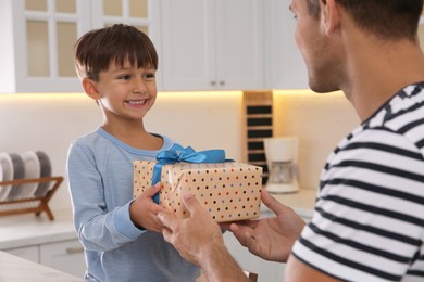 Photo of Man receiving gift for Father's Day from his son in kitchen