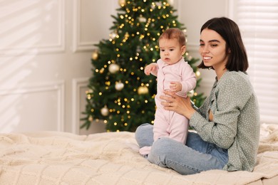 Photo of Happy young mother with her cute baby on bed at home, space for text. Winter holiday