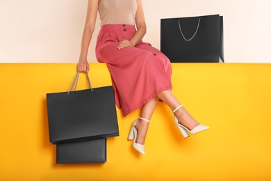 Woman with shopping bags sitting on yellow background, closeup. Black Friday