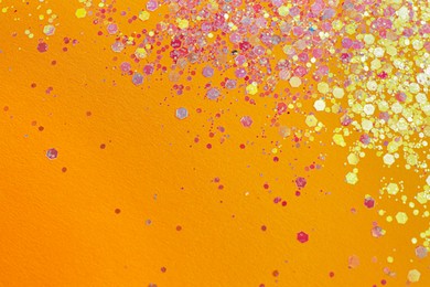 Photo of Shiny bright lilac glitter on orange background, flat lay. Space for text
