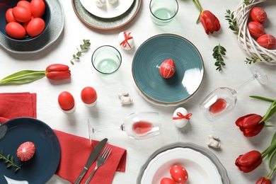 Festive Easter table setting with painted eggs on wooden background, flat lay