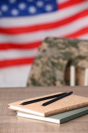 Notebooks and pencils on wooden table against flag of USA. Military education