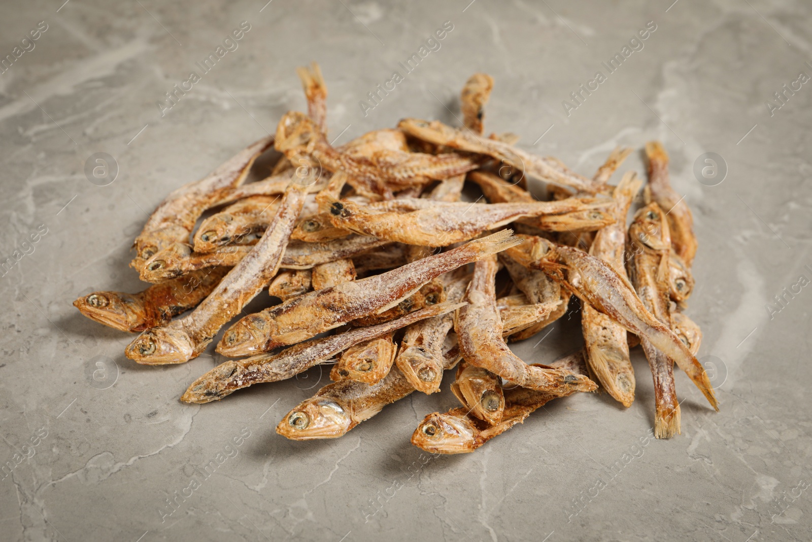 Photo of Heap of tasty dried anchovies on light grey marble table, closeup